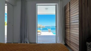 A bedroom with a view of the sea, a wooden bed, and a balcony with a table and chairs. - Villa NALA seaside pool standing, relaxation facing the lagoon feet in the water  (LE ROBERT)