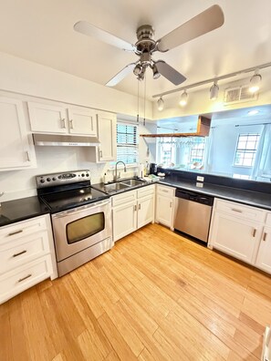 A modern kitchen with white cabinets, stainless steel appliances, and a wooden floor.