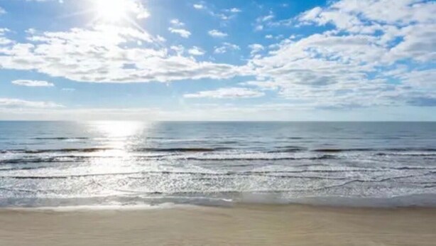 A beach with a clear sky and sunlight reflecting off the water.