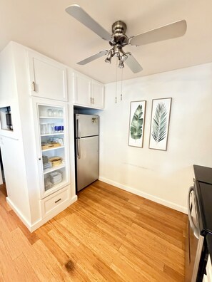 A kitchen with white cabinetry, a stainless steel refrigerator, wooden flooring, and a ceiling fan.