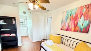 Een slaapkamer met een bed, een plafondventilator, een boekenplank en een schilderij aan de muur.