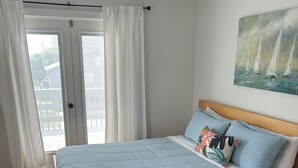 A bedroom with a bed, wooden floor, ceiling fan, and a painting on the wall.
