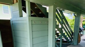 Een overdekt buitengebied met een groene houten constructie, een betonnen vloer en een trap die naar een hoger niveau leidt.