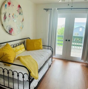Un dormitorio con una cama, almohadas amarillas, un cuadro redondo y un ventanal corredizo a un balcón.
