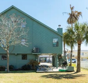 A single-story house with a green exterior, a covered patio area, and a small front yard with a palm tree.