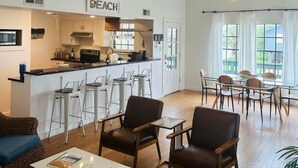 A spacious living area with a high ceiling, a kitchen with a bar, and a dining area with natural light from large windows.