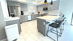 Una cucina moderna con mobili grigi, un frigorifero in acciaio inossidabile, un forno integrato e una grande isola con sgabelli da bar.