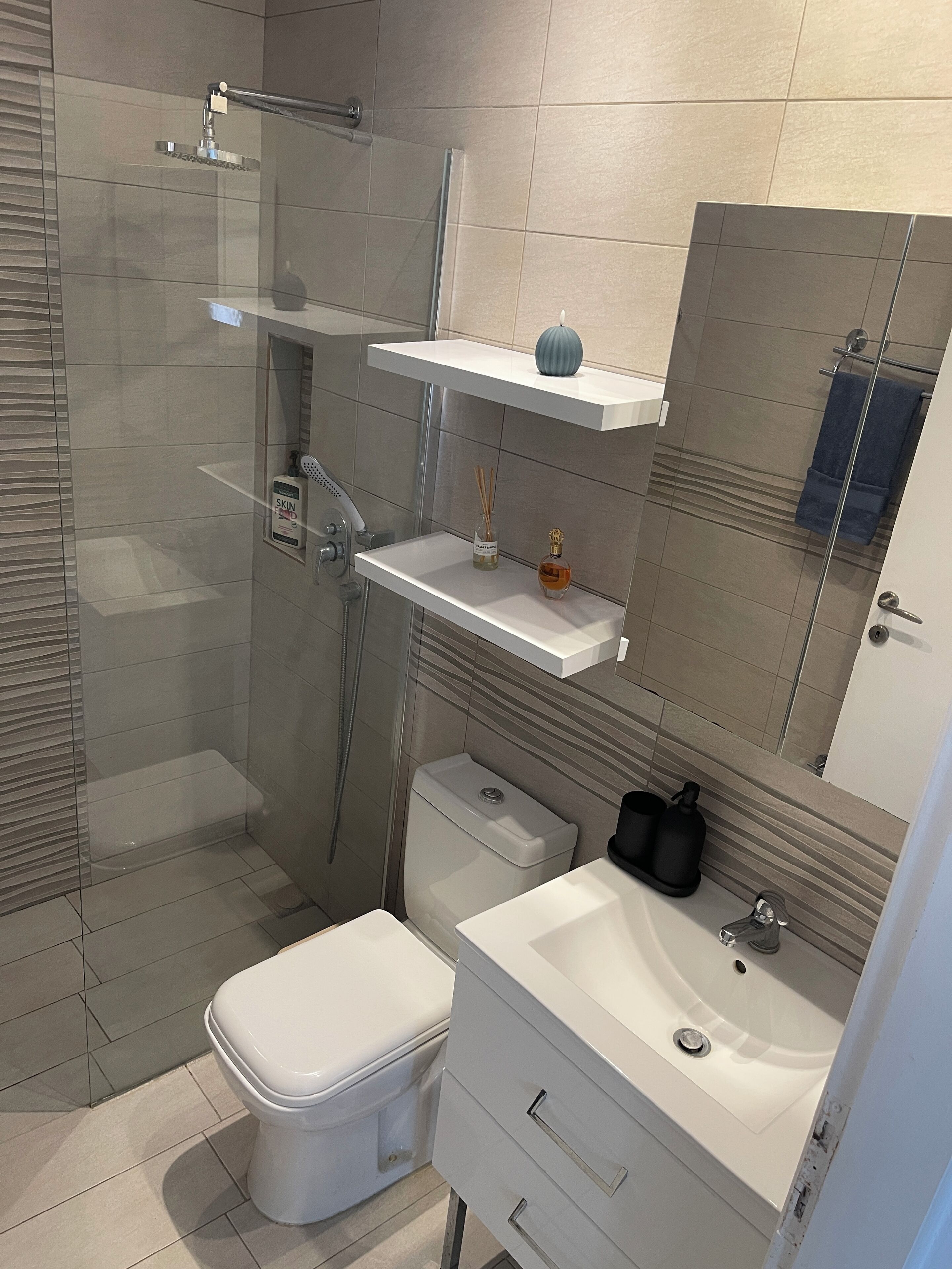 Ein modernes Badezimmer mit einer Glastrennwand-Dusche, Toilette, Waschbecken mit Spiegel und Ablage für Toilettenartikel.