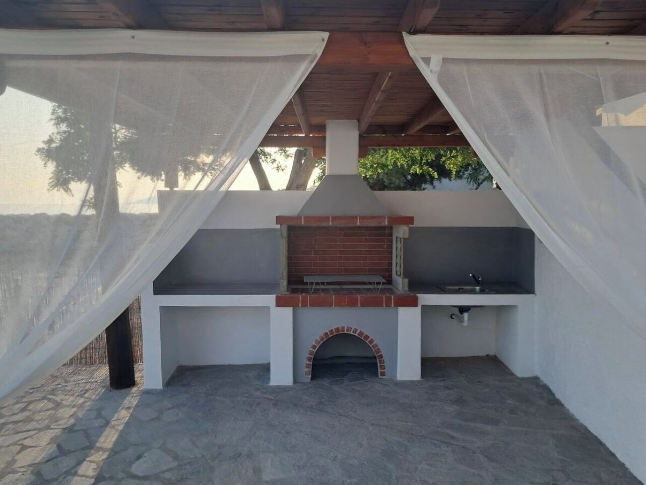 An outdoor kitchen area with a brick oven, a sink, and a window.
