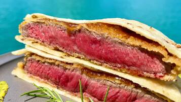 A stack of sandwiches with a sprig of rosemary on a plate, set against a scenic background of a turquoise sea and a green island.