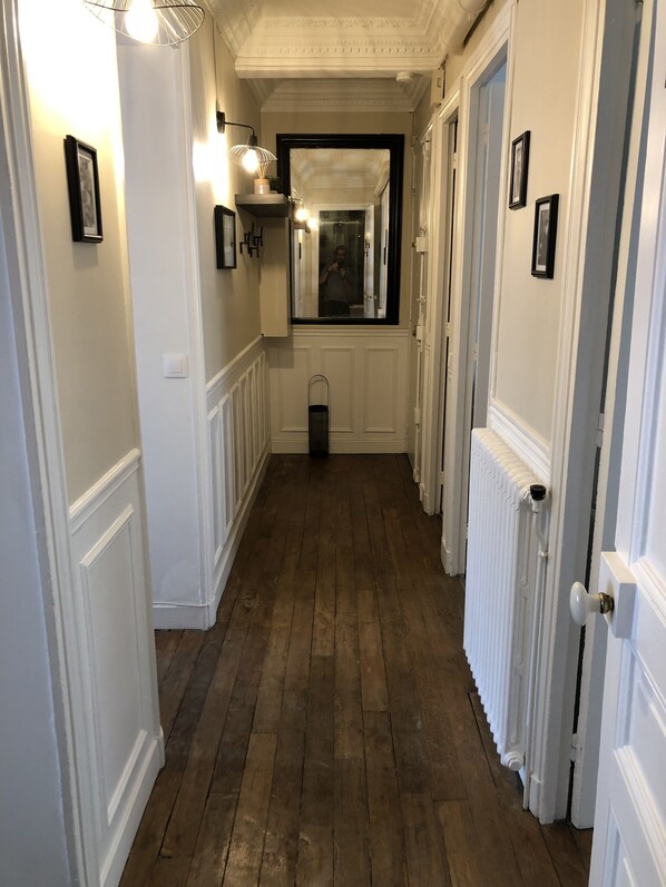 A narrow hallway with wooden flooring, white walls, and a radiator on one side.