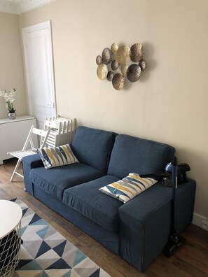 A living room with a blue sofa, white chairs, a patterned rug, and a decorative wall piece.