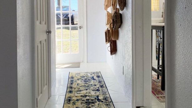 A hallway with a patterned rug, a white door, and a wall with hanging items. - Charming Country Cottage- Long Term Stays Welcome! (Eden)