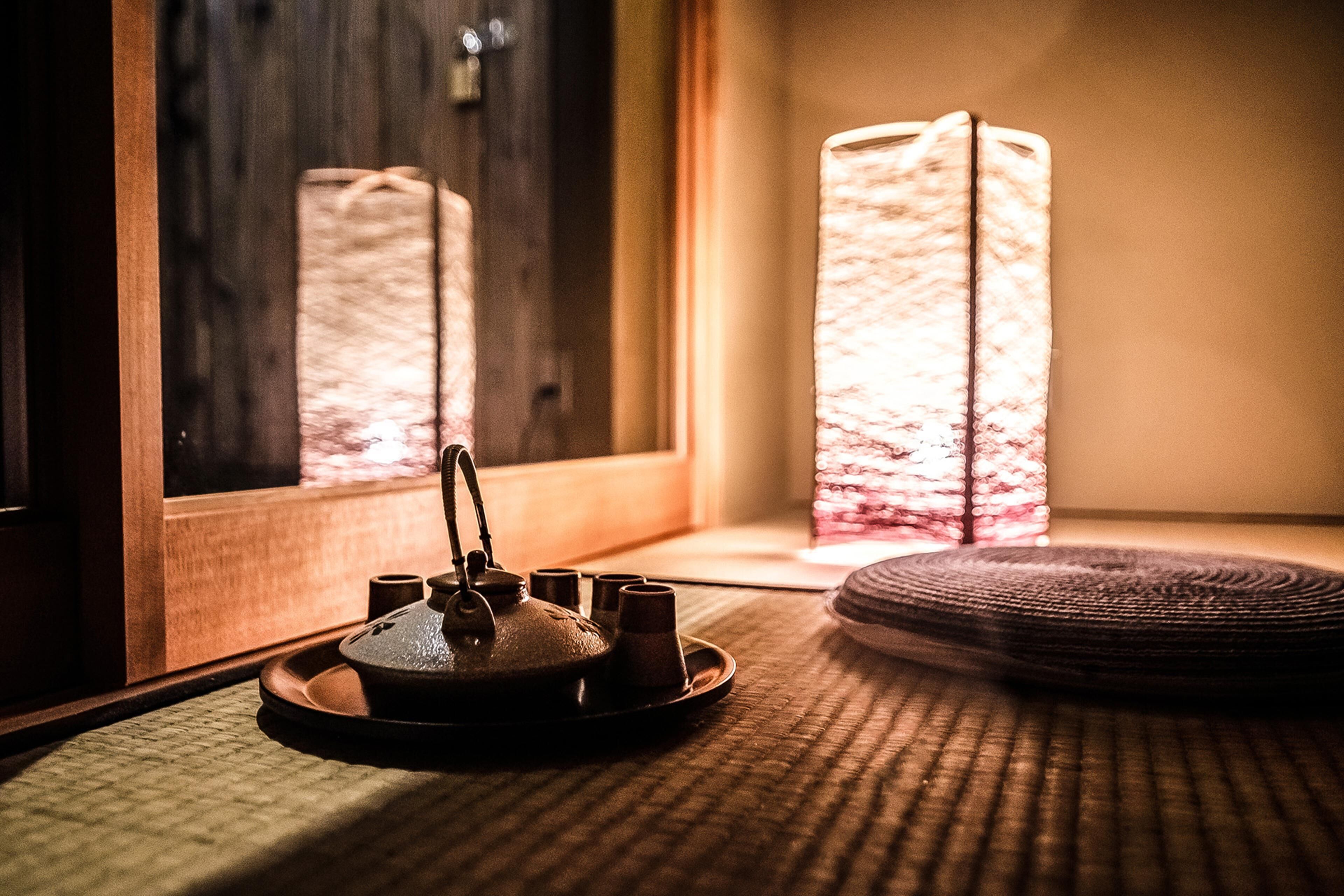 A traditional Japanese tea set on a tatami mat near a window with a view of a building.