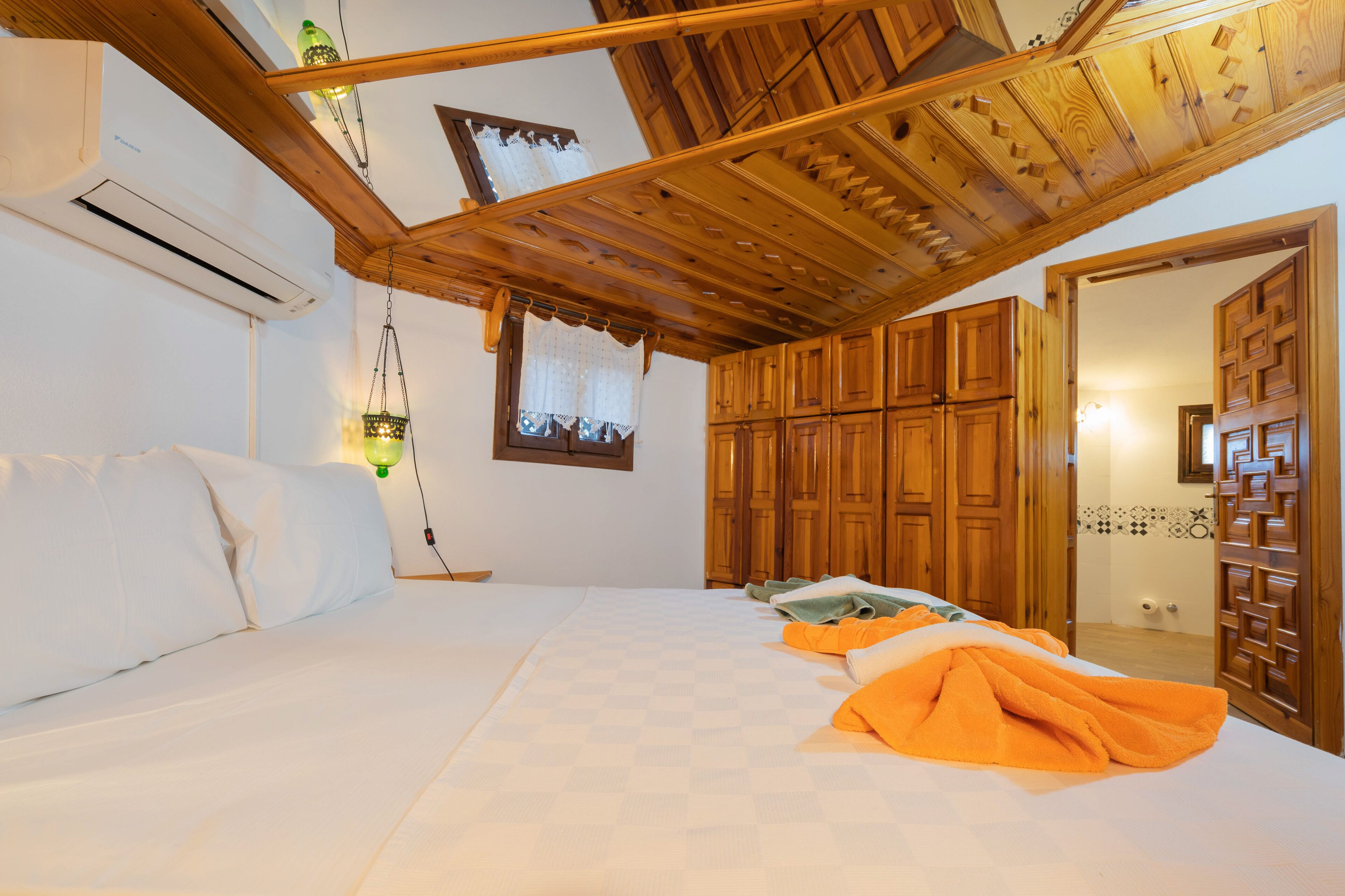 A bedroom with a bed, wooden wardrobe, and a ceiling with wooden beams.