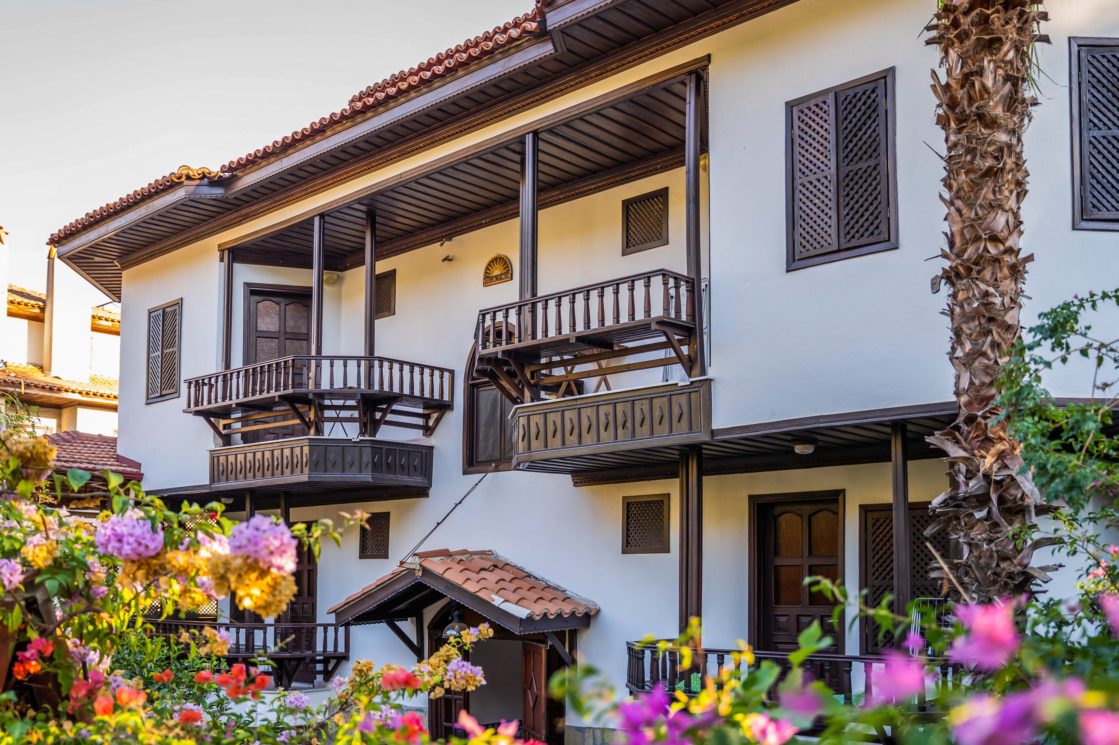 Un edificio de dos plantas con balcones, un pequeño porche y un jardín lleno de flores.