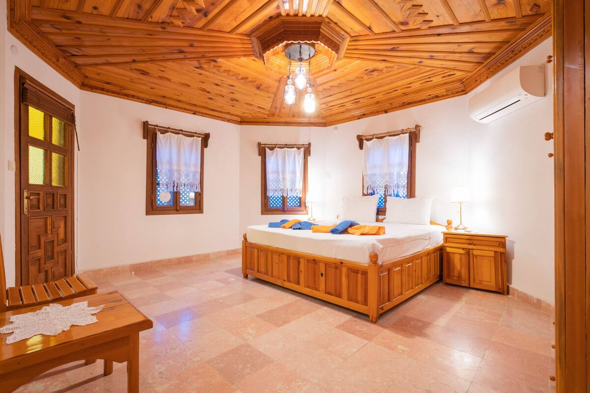 Een slaapkamer met een houten plafond, een groot bed, een nachtkastje en een bankje.