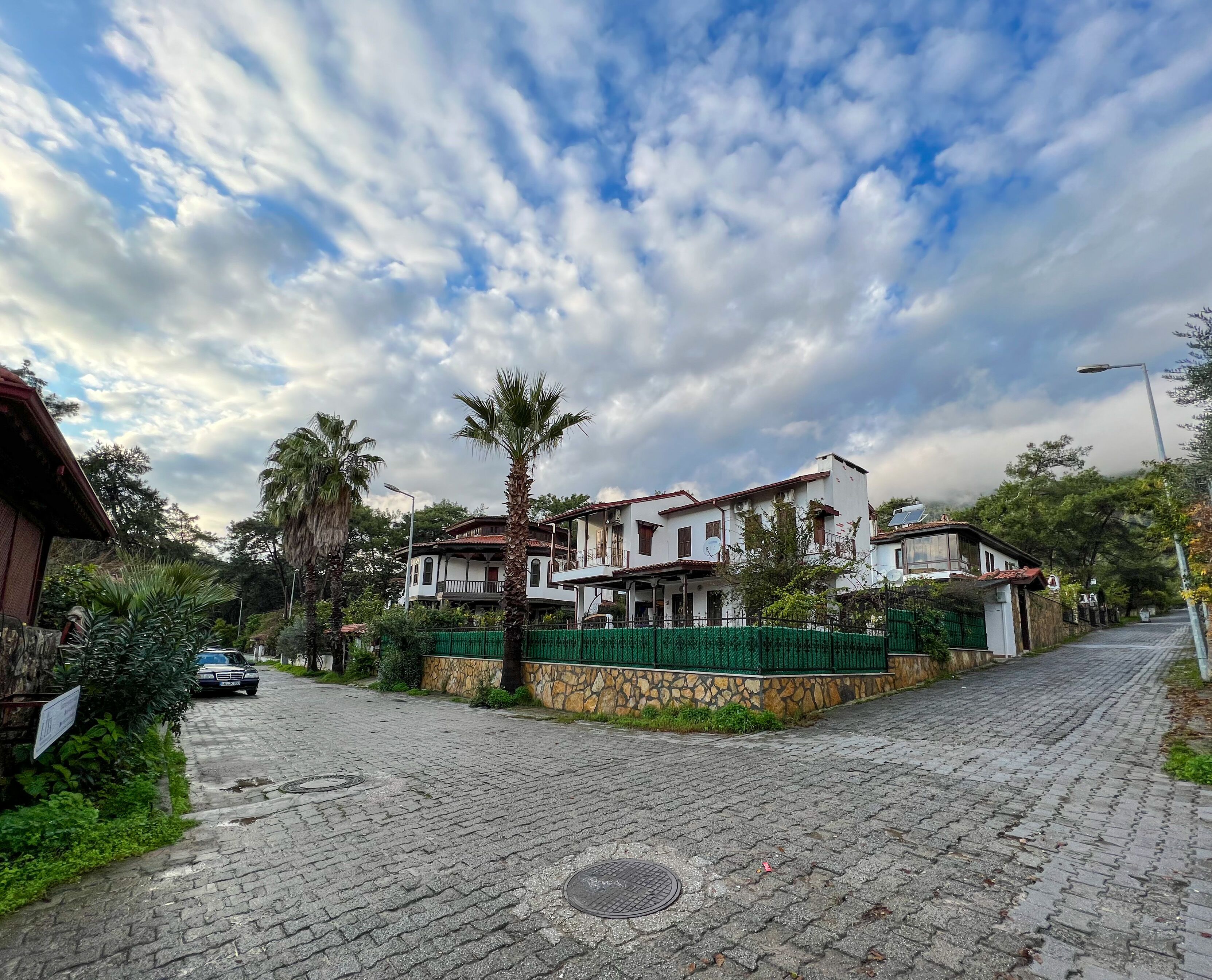 Una casa de dos pisos con fachada de piedra, un balcón y una cerca verde.