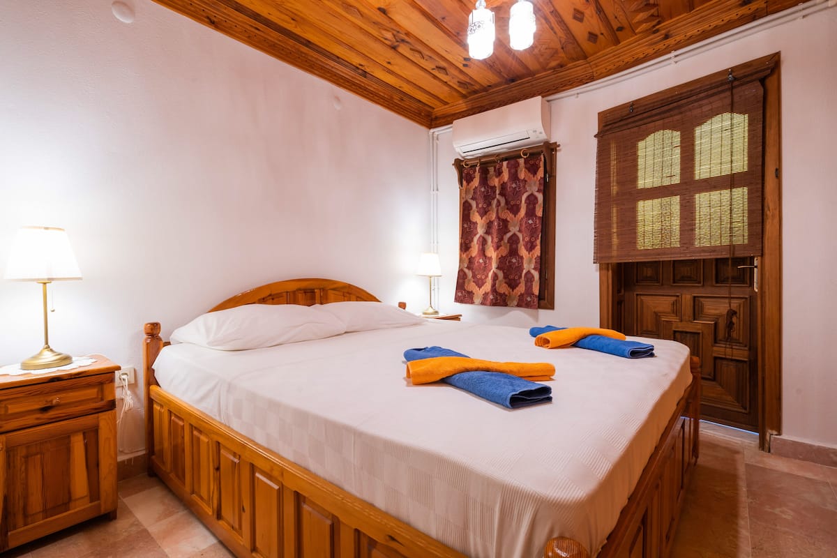 Een slaapkamer met een houten bed, twee nachtkastjes, een raam met een patroon gordijn en een airconditioning.
