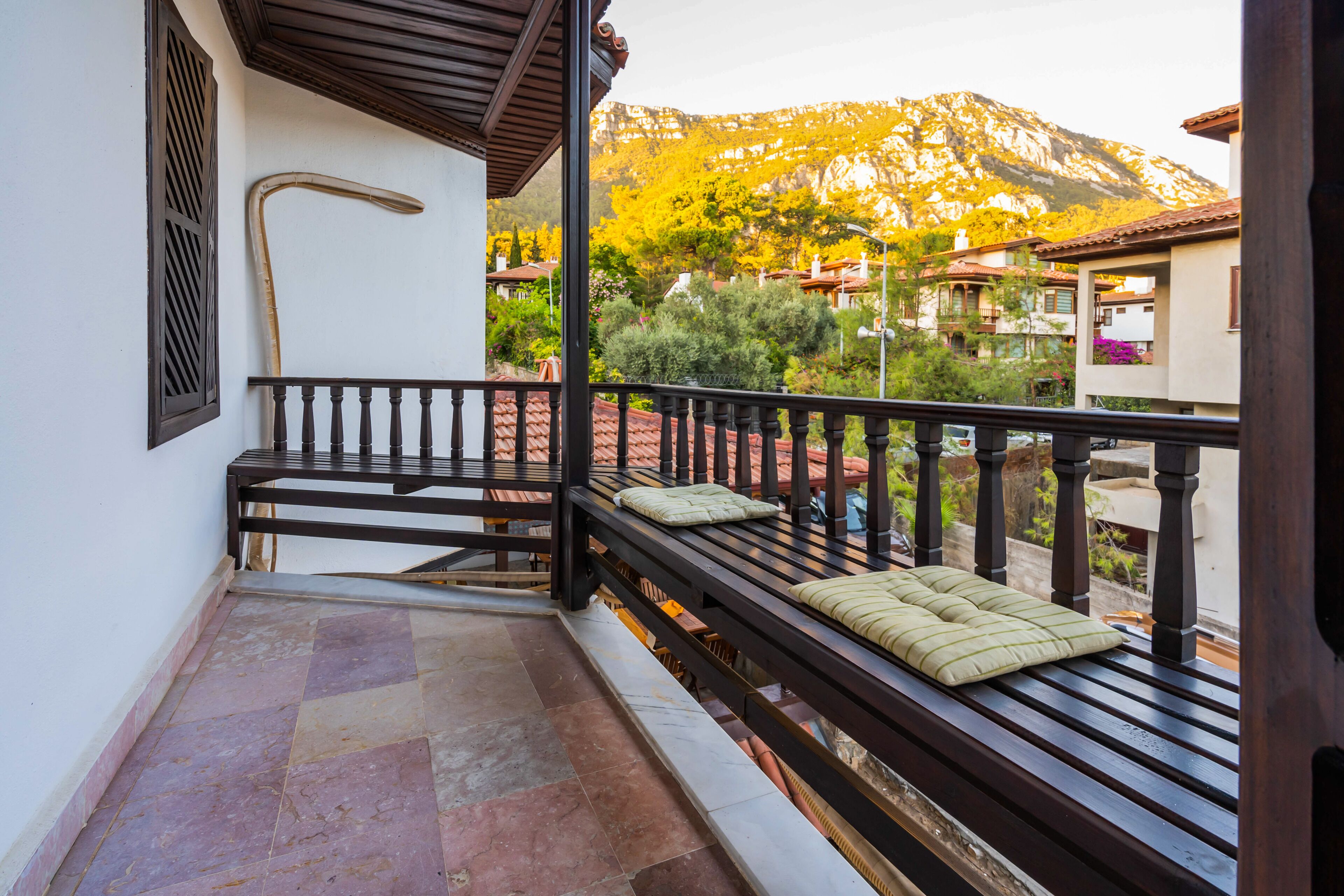 A balcony with a wooden bench, a cane, and a view of a mountain and buildings.