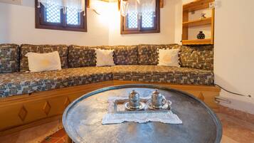 Una sala de estar acogedora con un sofá estampado, una mesa redonda de metal con dos saleros y un mantel de encaje.