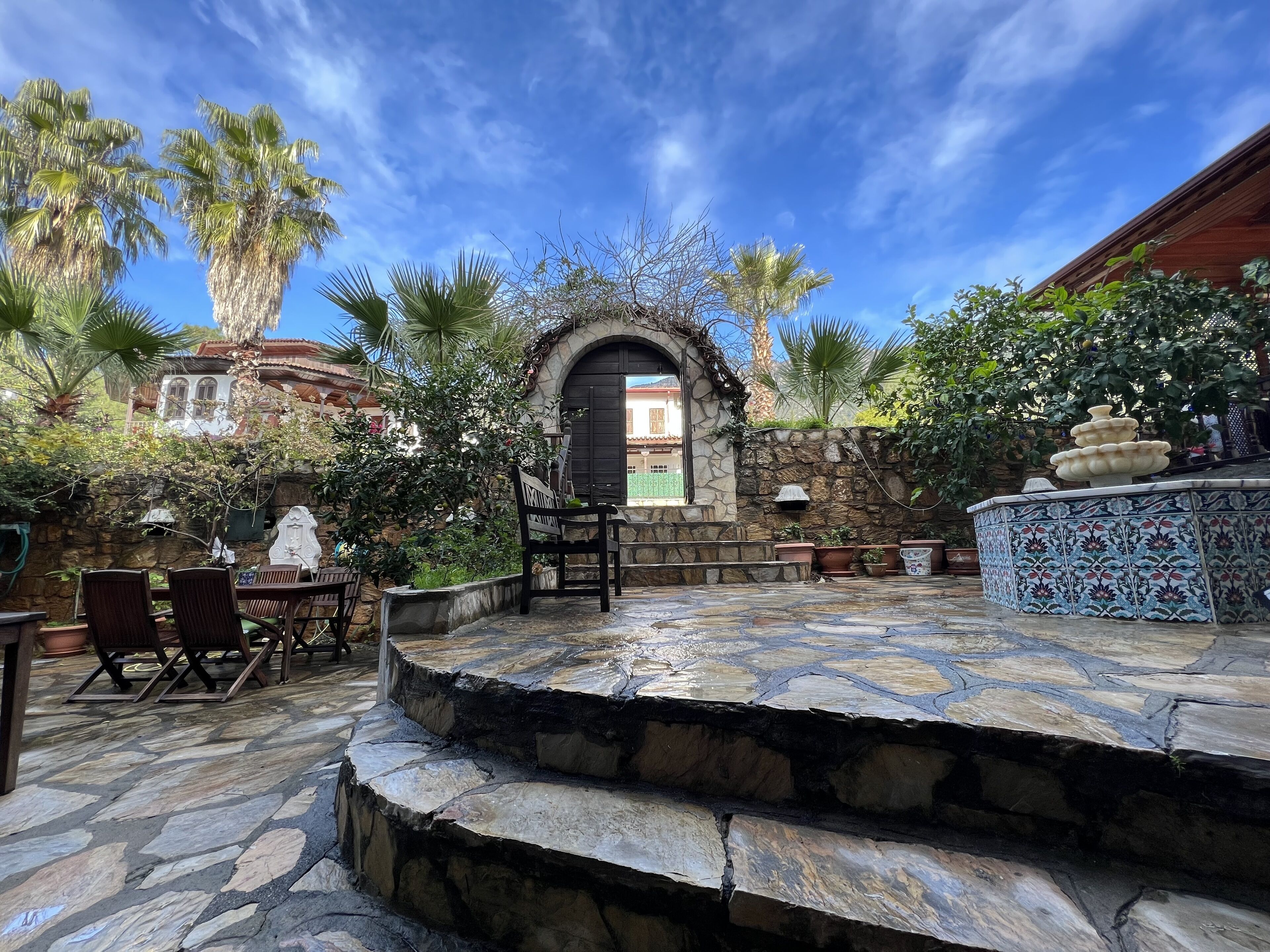 A stone patio with a fountain, surrounded by potted plants and a stone wall.