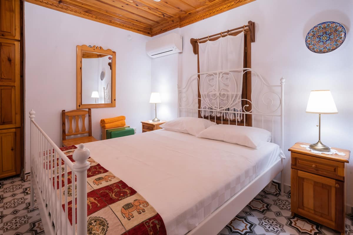 Een slaapkamer met een bed, een houten hoofdbord, een nachtkastje met een lamp, een spiegel en een kamerkleed met dessin.