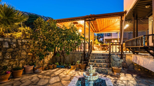 Un patio empedrado con una fuente, plantas en macetas y una pérgola de madera.