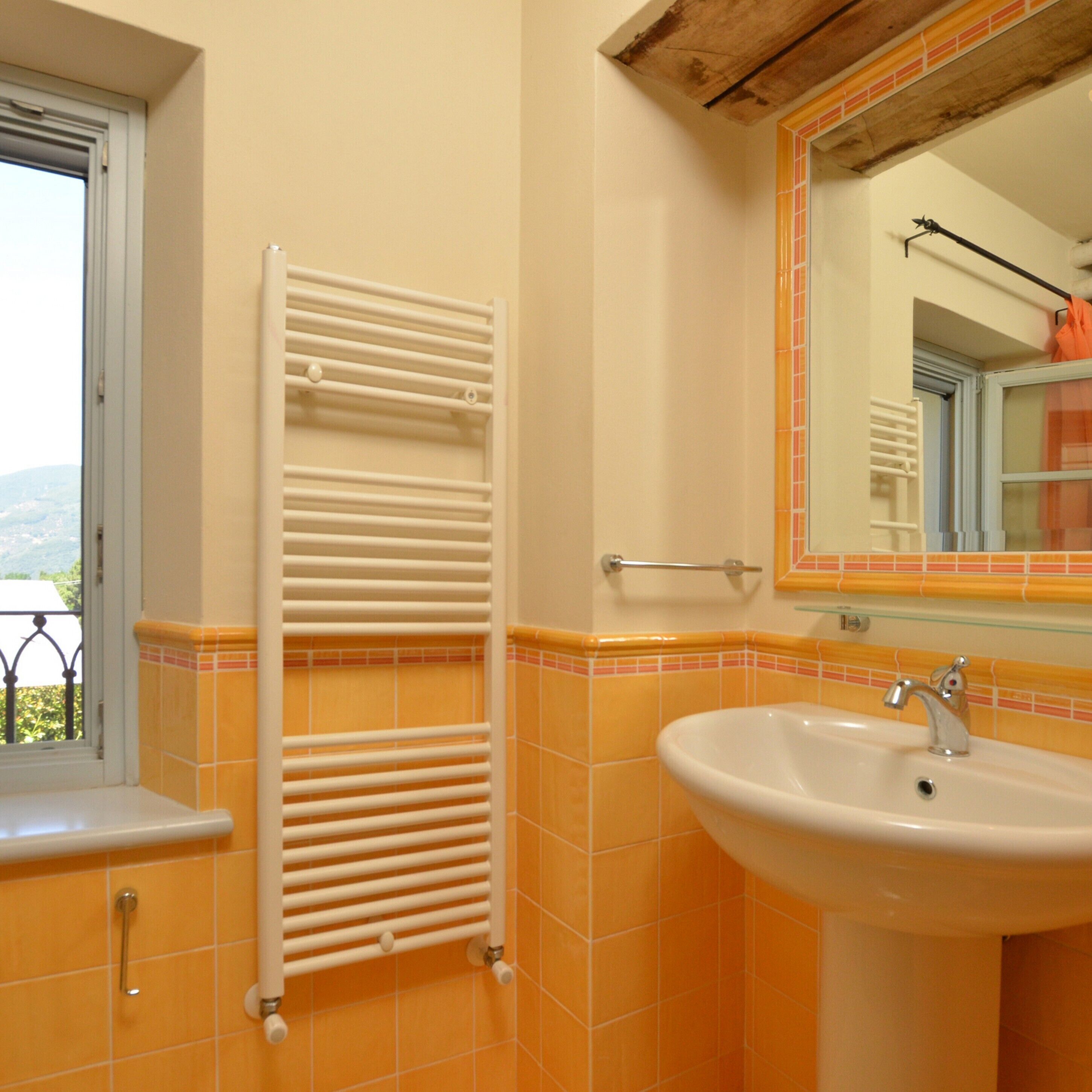A bathroom with a white towel rack, a sink with a mirror above it, and orange-tiled walls.