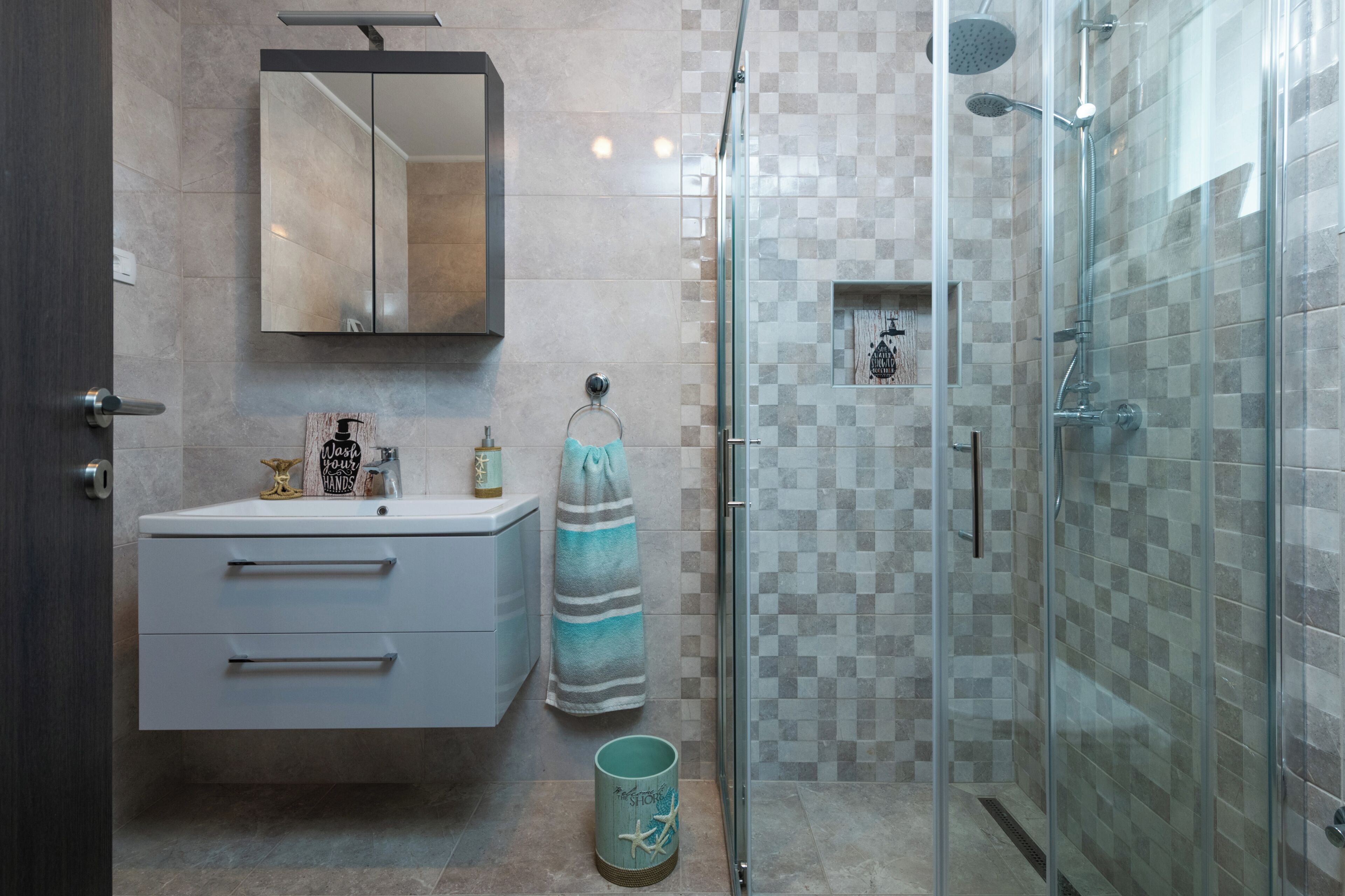 A modern bathroom with a glass shower enclosure, a white vanity with drawers, a towel rack, and a decorative mirror.