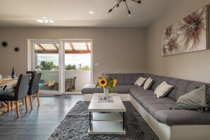 A modern living room with a grey sectional sofa, a white coffee table, and a dining area with chairs and a table.