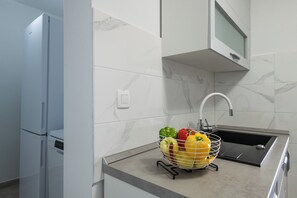 A kitchen with a marble backsplash, a sink, and a fruit basket on the counter.