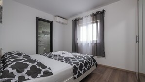 Camera da letto con un letto, un comodino, uno specchio, un condizionatore d'aria e una finestra con tende.