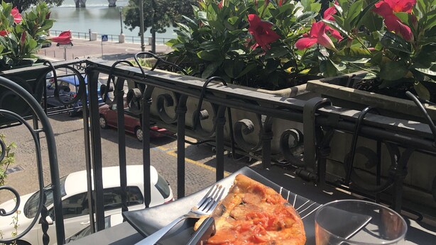 A table with a pizza, a fork, and a glass of red wine, overlooking a river with a bridge and buildings in the background. - Apartment La Piu' Bella Verona (Verona)
