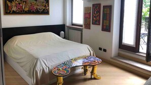 A bedroom with a bed, a colorful table, a painting, and a window with a view. - Apartment La Piu' Bella Verona (Verona)