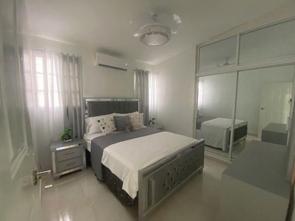 A bedroom with a bed, bedside tables, a nightstand, a dresser, a mirror, and a ceiling light fixture.
