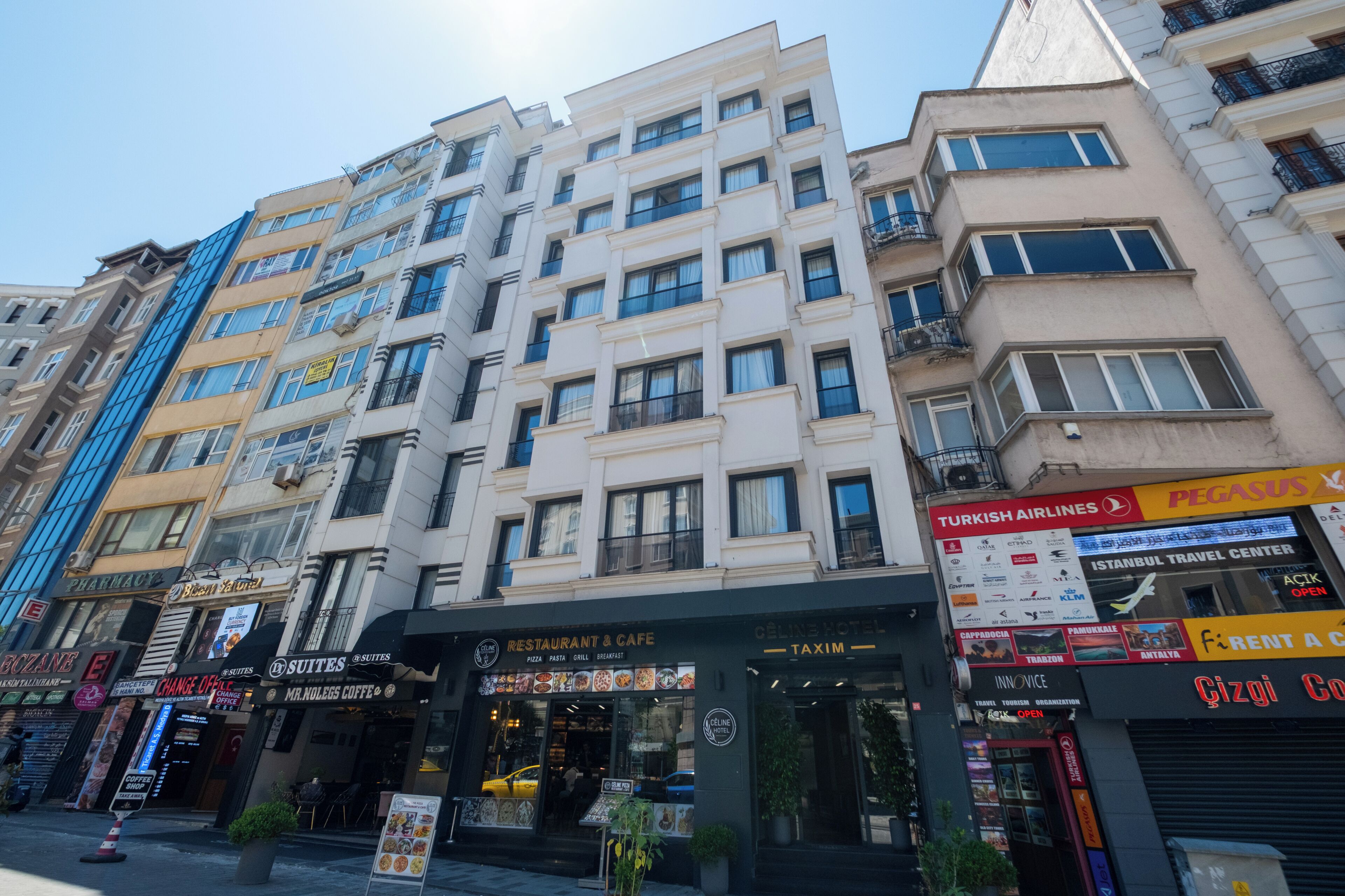 Un edificio a più piani con diversi esercizi commerciali al piano terra, tra cui un ristorante, una farmacia e un hotel.