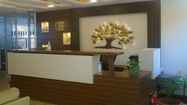 A reception desk with a wooden finish, a wall-mounted decorative tree, and potted plants. - Siri Delight (Bengaluru)