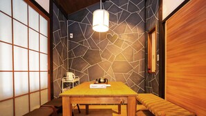 Une pièce avec une table en bois, des bancs, un luminaire suspendu et un mur orné d’un motif géométrique.