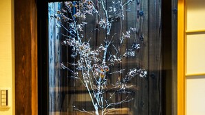 Un intérieur japonais traditionnel avec une porte en bois, une lanterne en pierre et un petit arbre placé près d’une fenêtre.