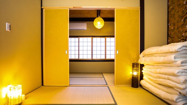 Une pièce de style japonais traditionnel, avec un sol recouvert de tatamis, une porte coulissante en papier de riz (shoji) et une pile de futons pliés.