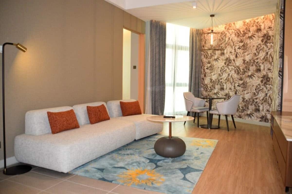 A modern living room with a sofa, chairs, a round table, and a patterned wall.
