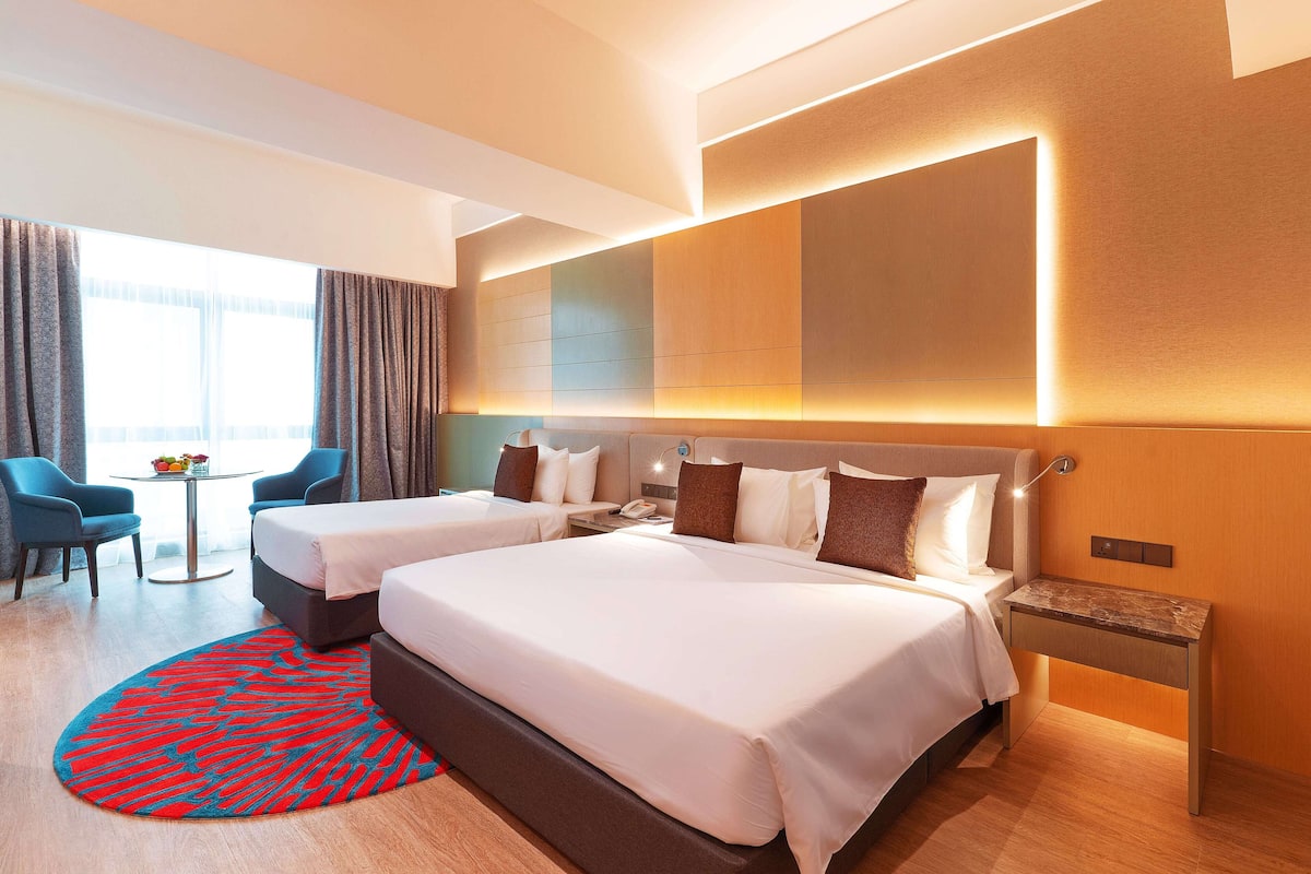 A hotel room with two beds, a desk, a chair, a round table, and a view of the outdoors.