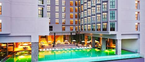 A modern hotel with a rooftop pool, multiple floors, and outdoor seating areas.