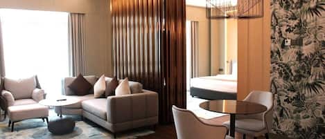 A modern hotel room with a sofa set, a round dining table, and a large window.