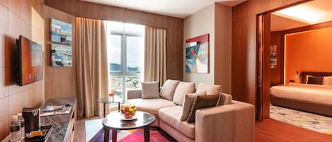 A modern hotel room with a sofa, a small table with a bowl of fruit, a TV, and a bed.
