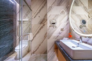Un baño moderno con ducha de vidrio, inodoro, lavabo con espejo y pared de azulejos de mármol.