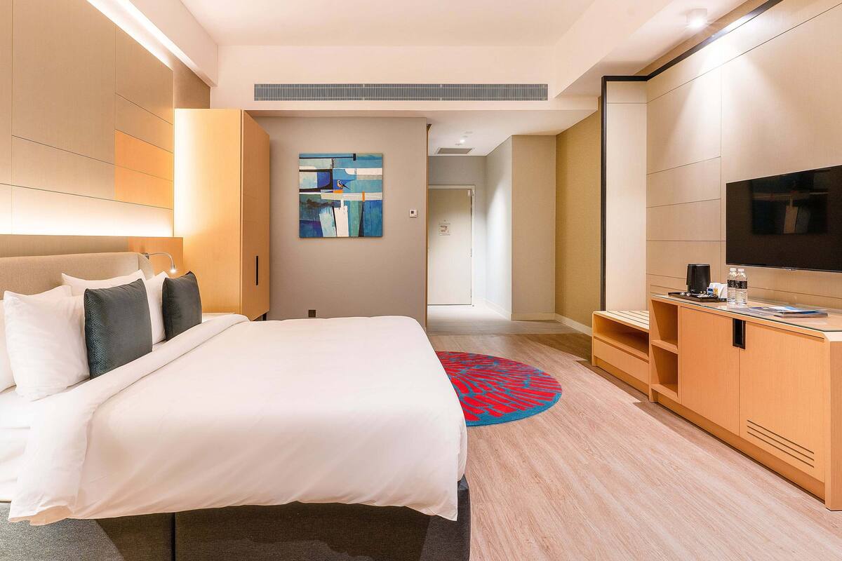 A hotel room with a large bed, a desk with a flat-screen TV, a coffee maker, and a small seating area.