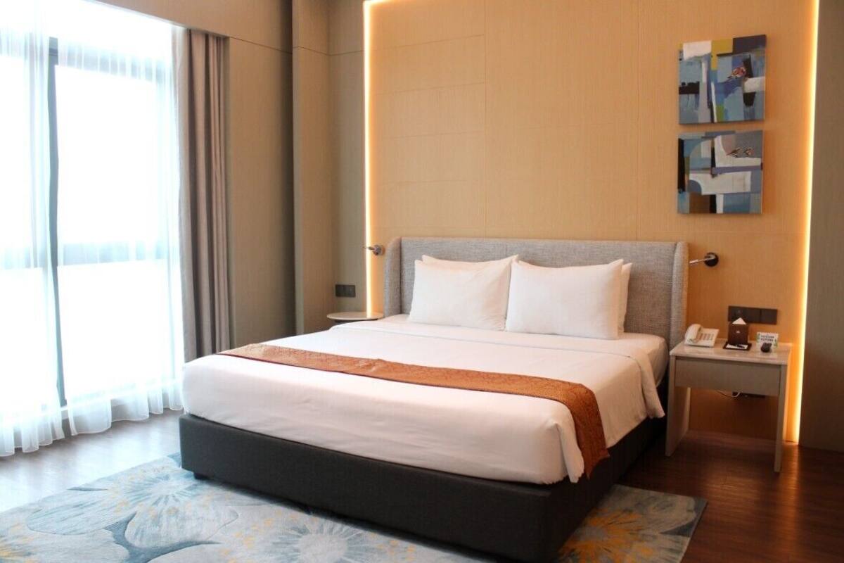 A hotel room with a large bed, a bedside table with a lamp, and a view of the outside through the window.