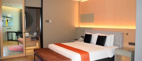 A modern hotel room with a large bed, a bench, a desk, and a mirror.